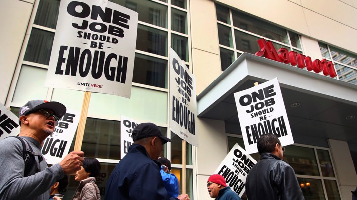 Hotel workers march and hold picket signs in front of a Marriott hotel.