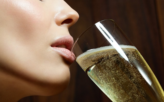 A woman brings a glass of champagne to her lips.