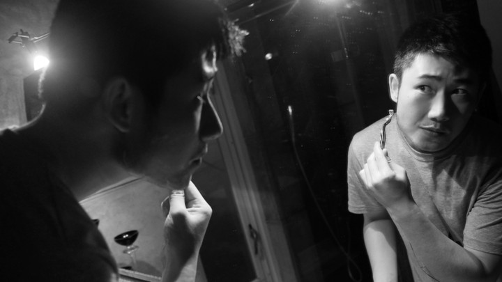 A young man shaves while looking in the mirror