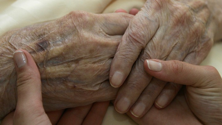 An elderly person holds hands with a younger person