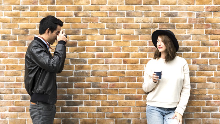 a man takes a photo of a woman against a brick wall - how to find out if girl follows you on instagram