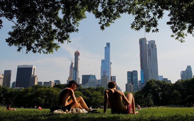 Two male figures recline on a grassy field. Manhattan's skyscrapers rise in the background.