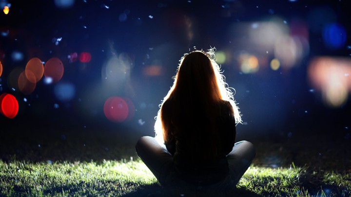 A girl sits in front of a blurry night sky