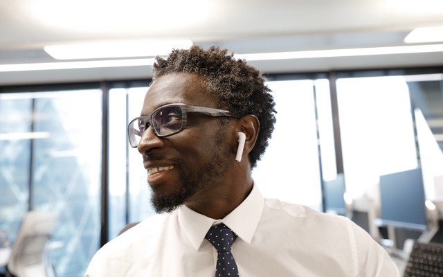A man wearing Apple AirPod headphones smiles in an office