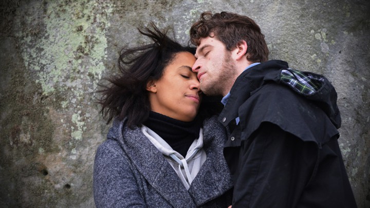 A man and a woman cuddle on a rock.
