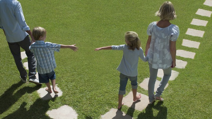 A man and woman lead two small children away from each other by the hand.