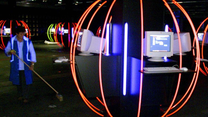 A person cleans up in a room full of computers and neon lights.