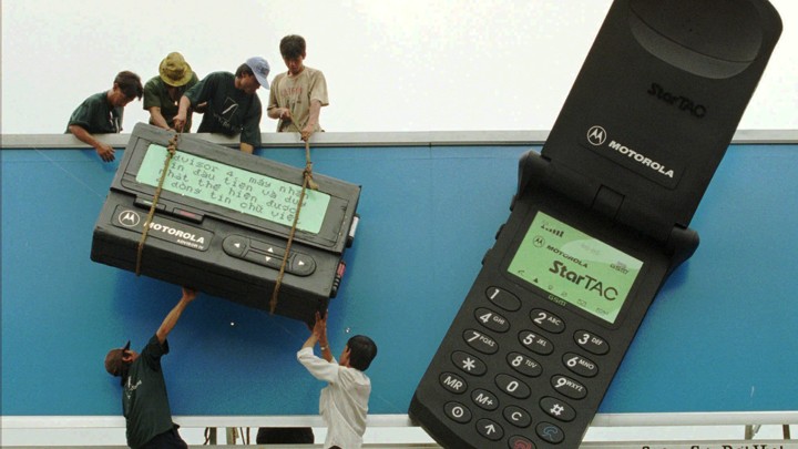 Workers hoist a giant Motorola cellphone and pager onto a billboard.
