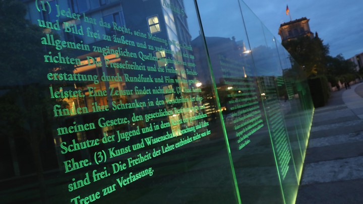 Articles of Germany's Basic Law (Grundgesetz), including article 5, which guarantees freedom of expression, the arts, and the press, stand illuminated on a glass wall in Berlin.