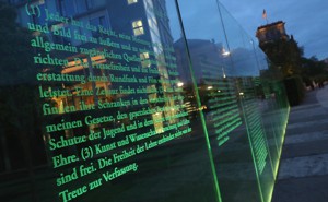 Articles of Germany's Basic Law (Grundgesetz), including article 5, which guarantees freedom of expression, the arts, and the press, stand illuminated on a glass wall in Berlin.