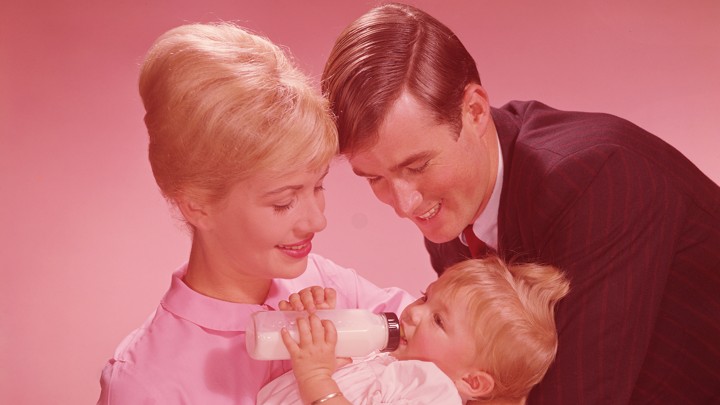 An archival photo of a mother holding a baby girl while the father looks on