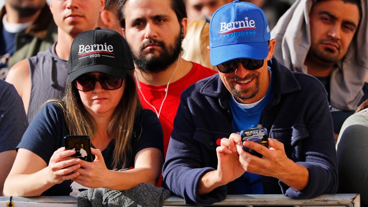 Bernie Sanders supporters look down at their phones during a rally.