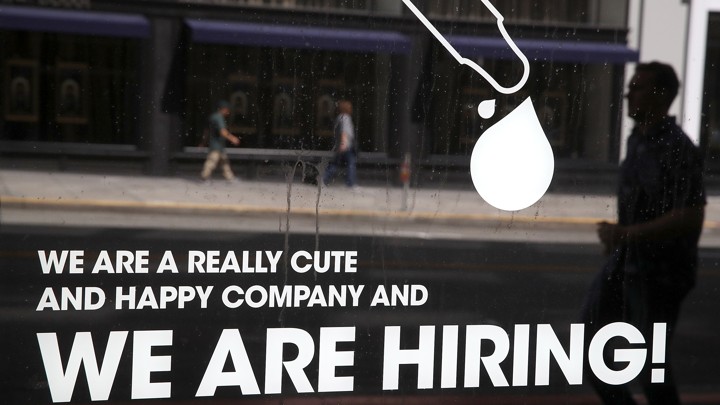 A man walks by a window with a hiring ad printed on it.