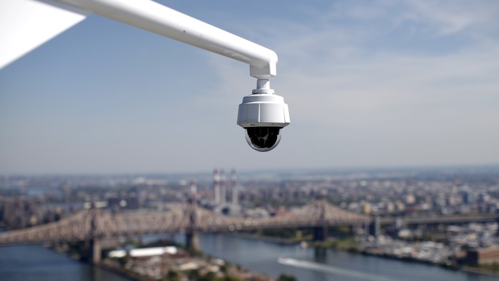 A security camera hangs from the roof of the Secretariat Building at the United Nations headquarters with the East River and Queensboro Bridge in the background in New York City.