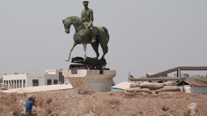 A Kurdish fighter fires a weapon at a statue of Bassel al-Assad, Bashar al-Assad's brother, in Hasaka, Syria, in August 2016.