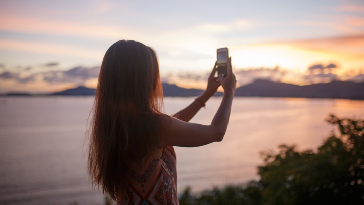 A woman takes a photo of a sunset.