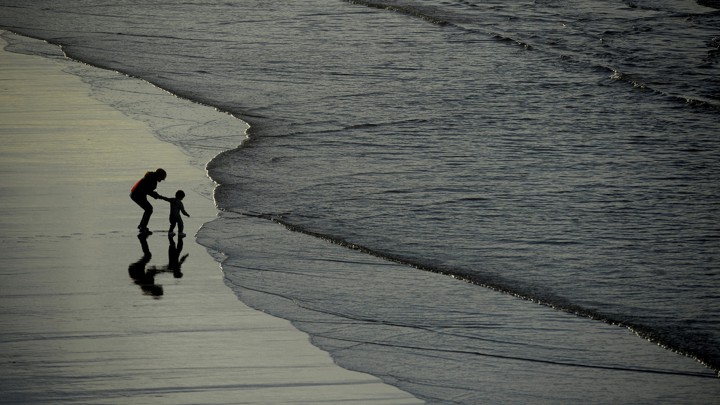 Silhouettes of a woman and a boy walking on a beach in Spain