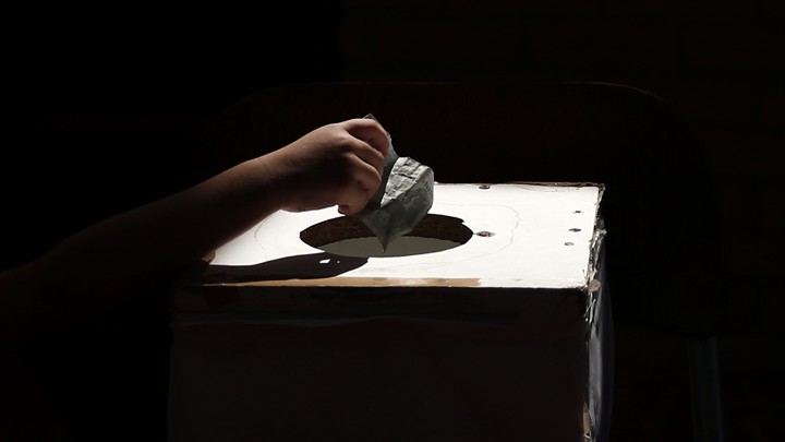 A hand drops money into a box.