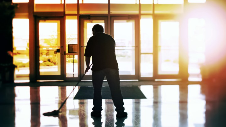 A custodian mops a floor in an office building at sunset.