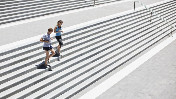 A man and woman jog down cement stairs together.