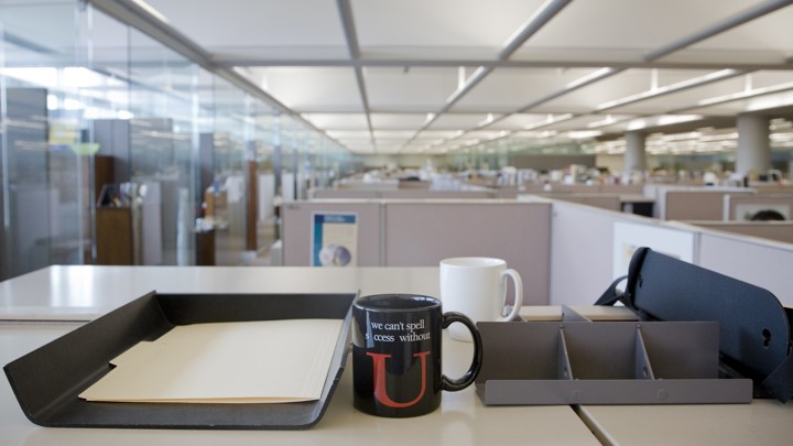 A mug sits on a desk in an office. The mug reads "We can't spell success without U."