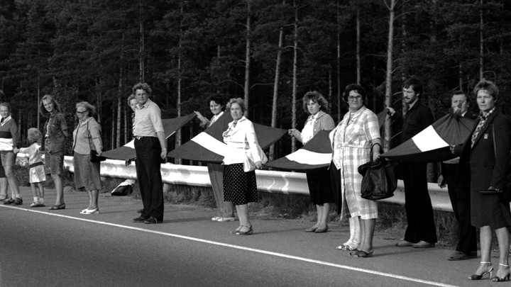 A group of people stand in a line holding hands with Latvian flags.
