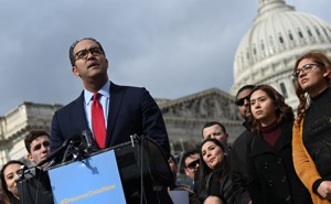 Representative Will Hurd of Texas stands at a podium outside the U.S. Capitol in Washington, D.C. Behind him are 10 men and women watching him speak. The Capitol dome is visible in the background.