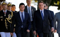 Sérgio Moro and Jair Bolsonaro walk with marines at a military ceremony.