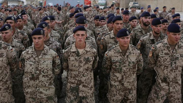 Ranks of German soldiers in military camouflage face the camera with sober expressions.