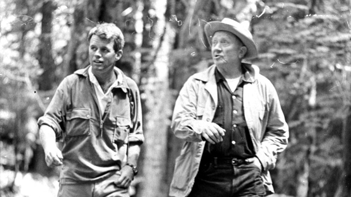 Robert F. Kennedy and Supreme Court Justice William O. Douglas hiking through the woods wearing outdoors gear.