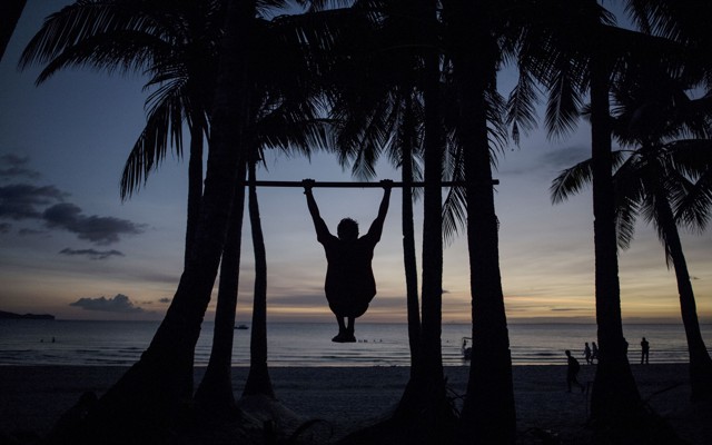 The silhouette of a man doing a pull-up on a beach in the Philippines.
