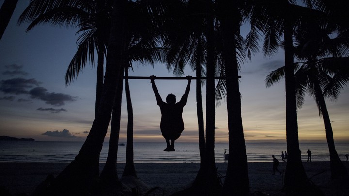 The silhouette of a man doing a pull-up on a beach in the Philippines.