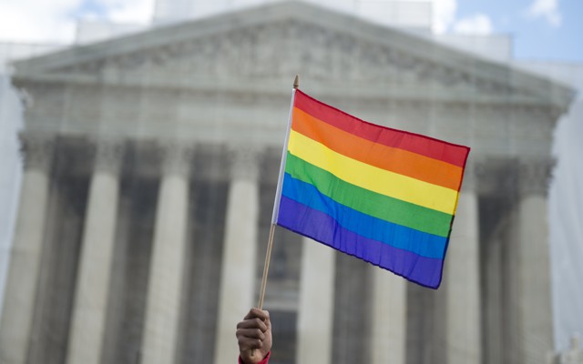 A hand holding a rainbow flag outside of the Supreme Court