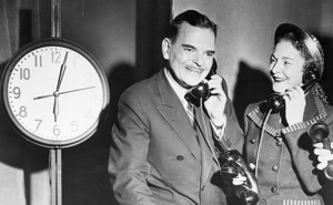 Two people talk on phones in front of a clock.