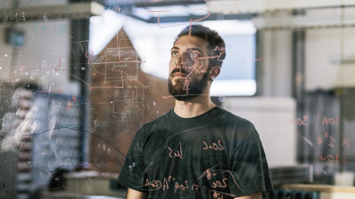 A young man stares at a markerboard covered in code