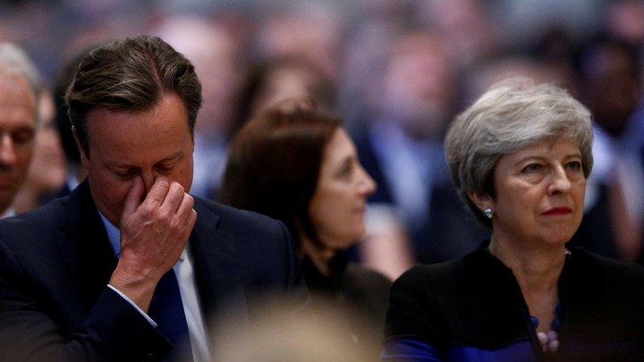 David Cameron holds his hand to his eyes as he sits alongside Theresa May at Westminster Abbey.