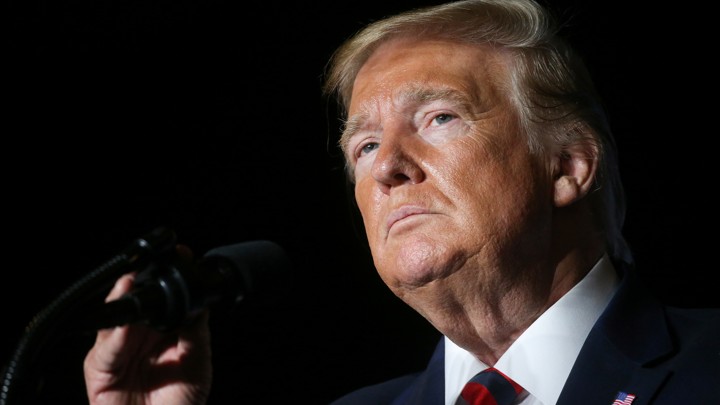 Donald Trump stands at a podium, adjusting the microphone.