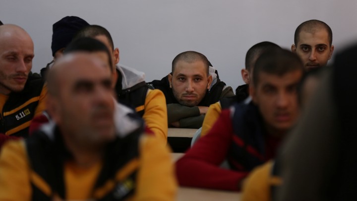 Former ISIS members sit at desks in a classroom.