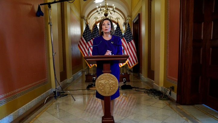 Nancy Pelosi stands in front of American flags and a lectern at the Capitol.