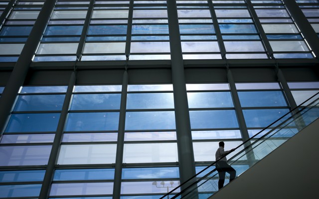 A man on an escalator looks at an enormous set of windows.
