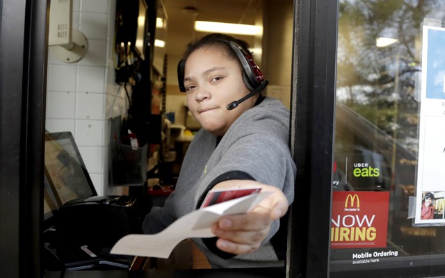A McDonald's worker at a drive-through hands someone behind the camera a receipt.