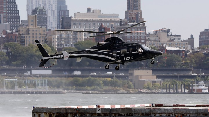 An Uber Copter lands at the Downtown Manhattan Heliport, in sight of buildings and the water.