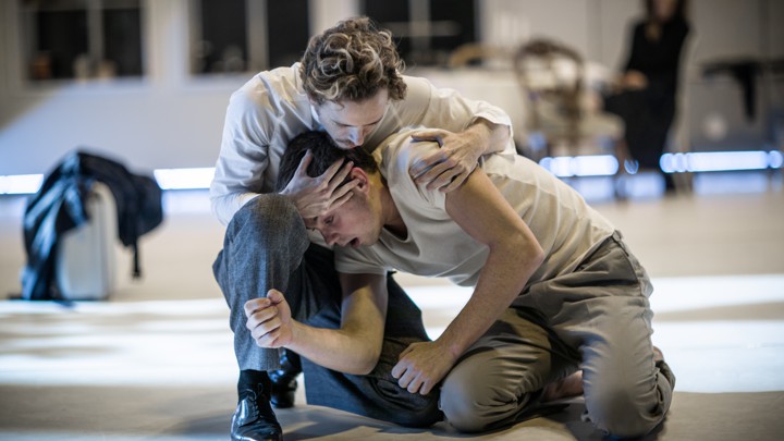 Two men in white clothes embrace on a stage.