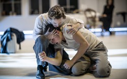 Two men in white clothes embrace on a stage.