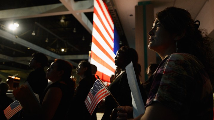U.S.-citizenship candidates look at a video presentation as they wait to take the oath of citizenship at a naturalization ceremony.