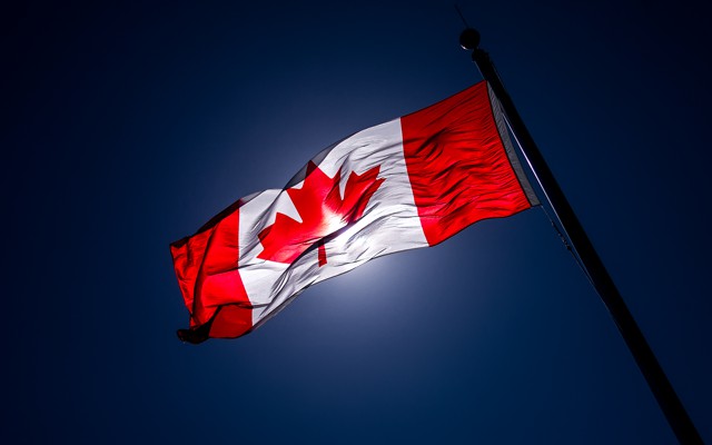 A Canadian flag, slightly darkened by the light, waves in the air.