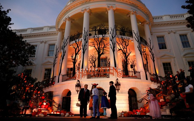 Trump passes out candy in front of a halloween-decorated White House.