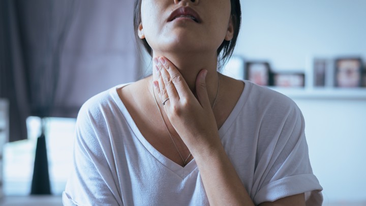 A young woman holds her neck in pain.