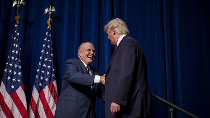 Rudy Giuliani and Trump shake hands in front of two American flags.