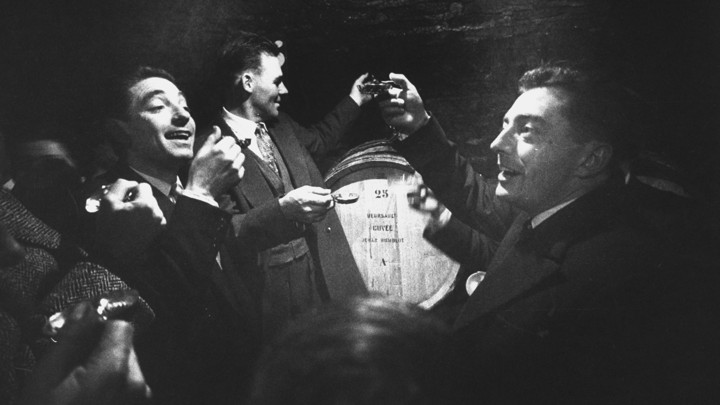 A black-and-white photograph of men in tuxedoes in a wine cave